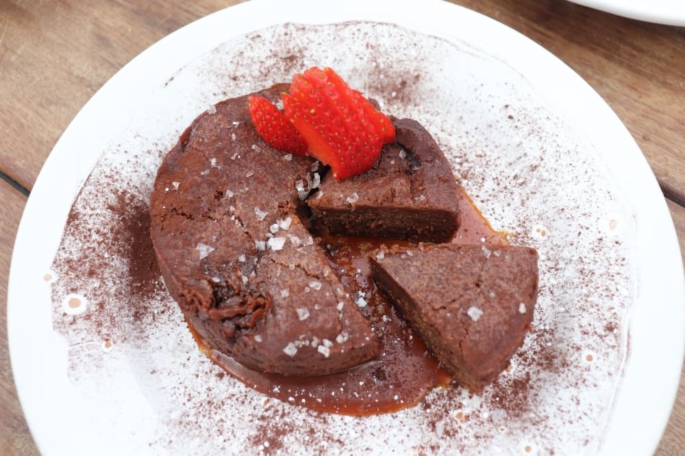 
The Chocolate & Caramel Argument is a flourless chocolate cake topped with strawberries on caramel sauce. 