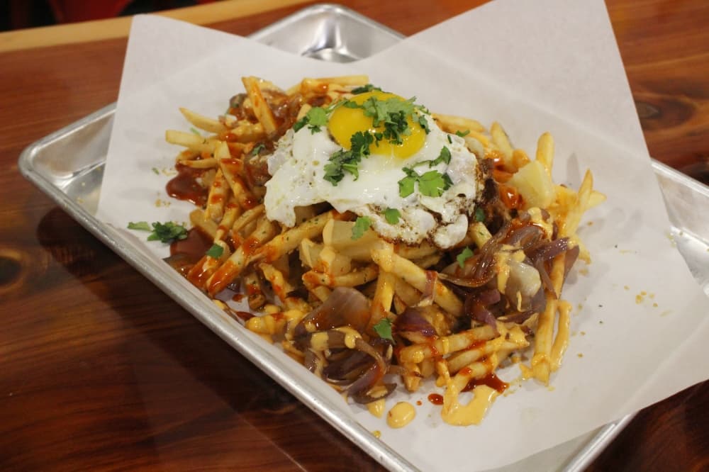 Nom Fries ($8.95) are topped with a choice of protein, grilled onions, pineapple and more. (Jackson King/Community Impact)