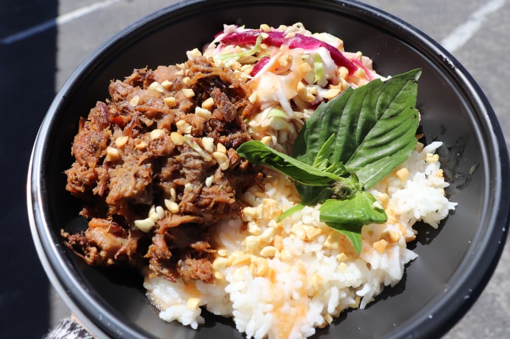 The rice bowl with chopped barbecue, purple kraut slaw, rice wine vinaigrette, fresh herbs, hot sauce and peanuts is shown. (Zara Flores/Community Impact Newspaper)