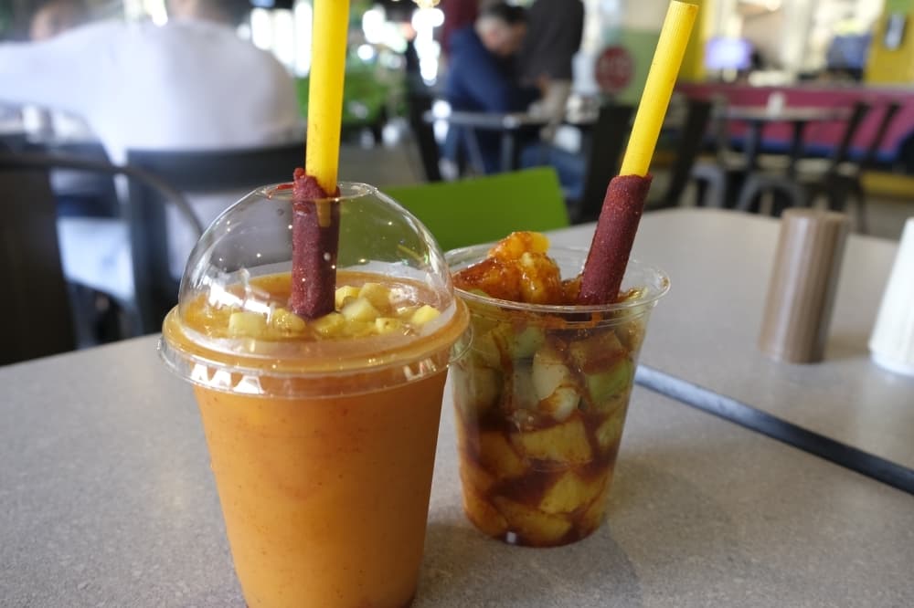 Mangonada ($4.79): Tinja Mango slush is served with a spicy mango lollipop straw (left). | Spicy Fruit ($3.69): The drink is made with a mix of mango, orange, pepino and chamoy. (George Wiebe/Community Impact Website)