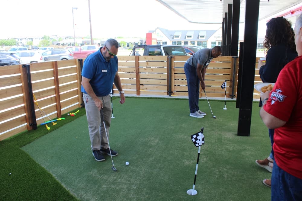 Grapevine Chamber of Commerce members play miniature golf on the Chicken Express lawn at the ribbon-cutting event. (Samantha Van Dyke/Community Impact Newspaper)