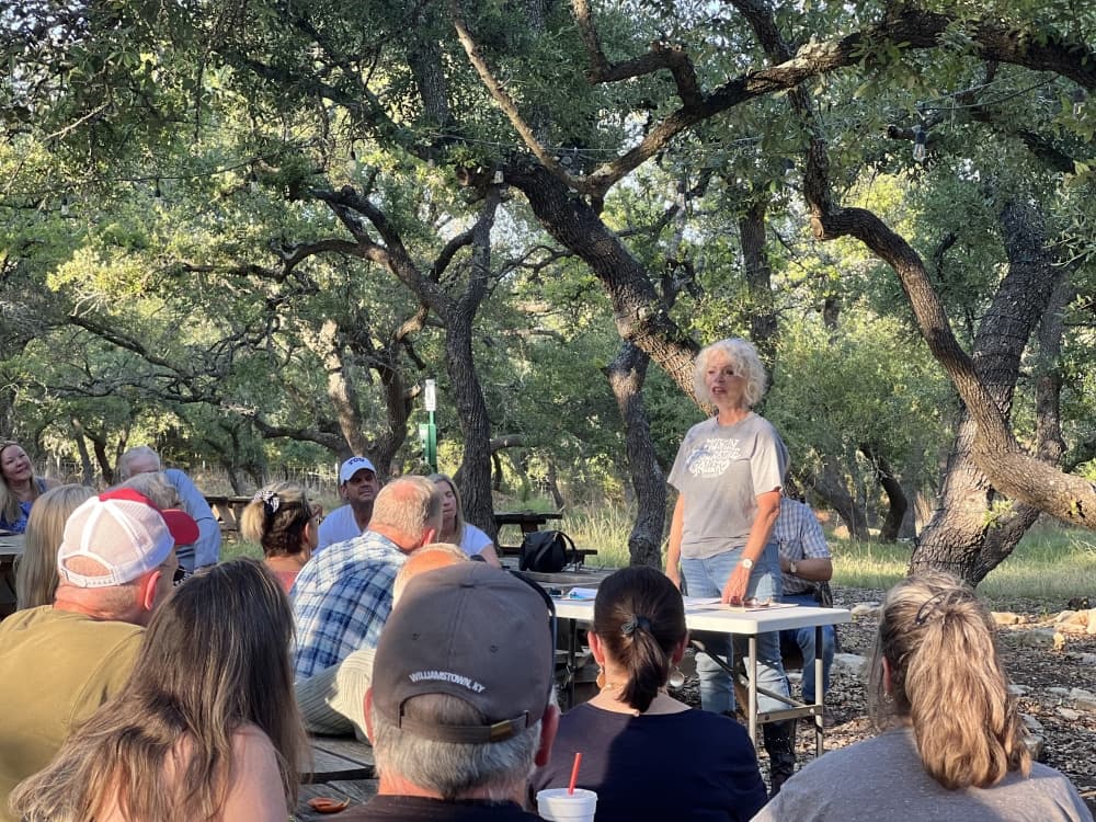 Woman standing at table outdoors in front of crowd