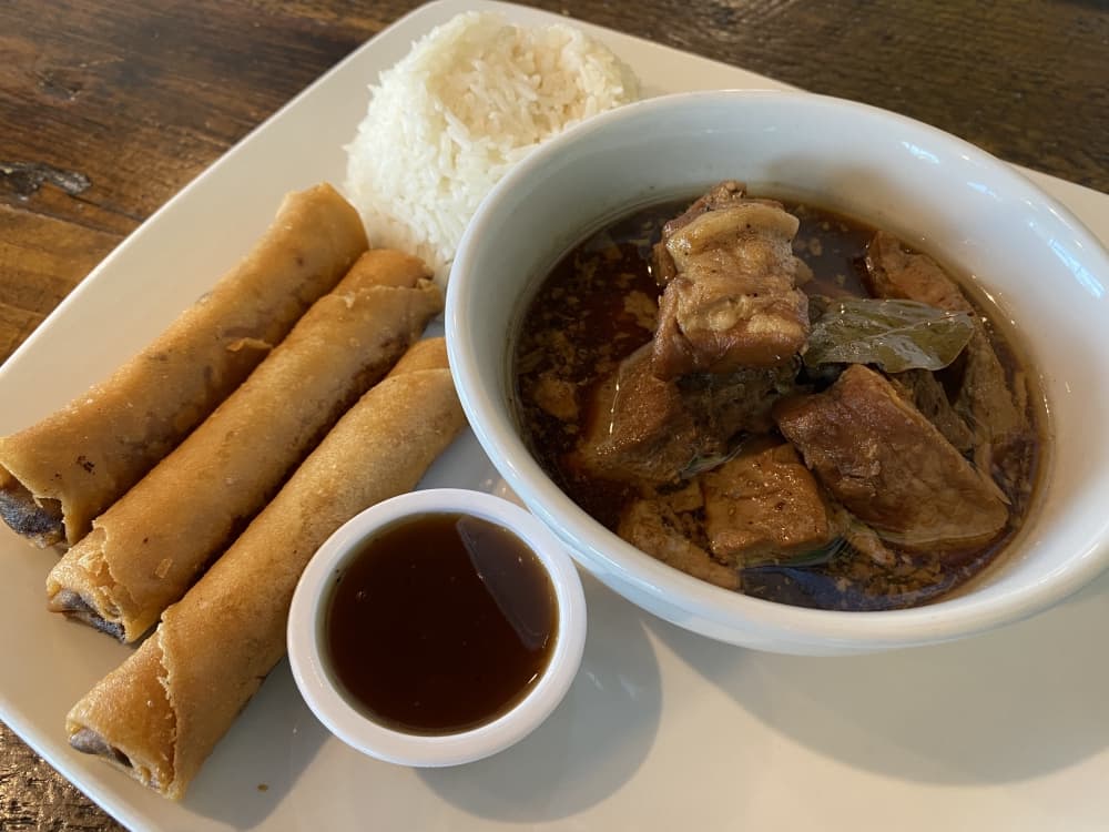 Pork adobo is pork loin cooked in vinegar-based broth, and it comes with three egg rolls.