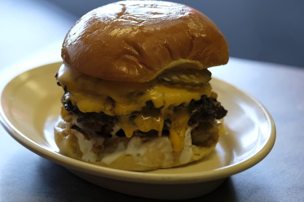 Loaded cheeseburger ($8.50): A cheeseburger is served with battered and fried onion, jalapeno slices, ranch drizzle, pickles and sauce. (George Wiebe/Community Impact Newspaper)