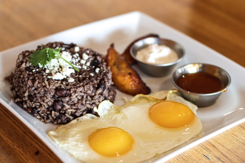 Jason's Foreign Breakfast ($11.50) consists of two eggs any style with newlywed rice and beans (white rice mixed with black beans) and is served with sweet plantains, fresh cheese, sour cream and a side of salsa. (Grant Johnson/Community Impact Newspaper)