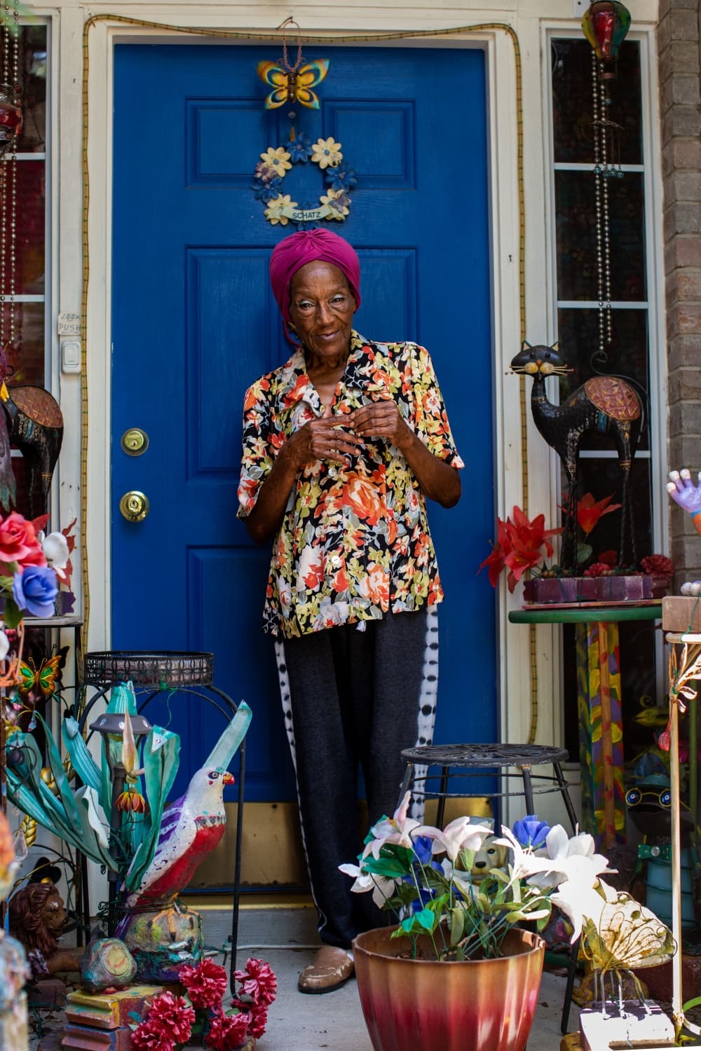 Mamie Schatz stands in front of her home, surrounded by dozens of unfinished painting projects that will eventually take their place in her colorful front yard. Credit: Kaylee Greenlee Beal 2022