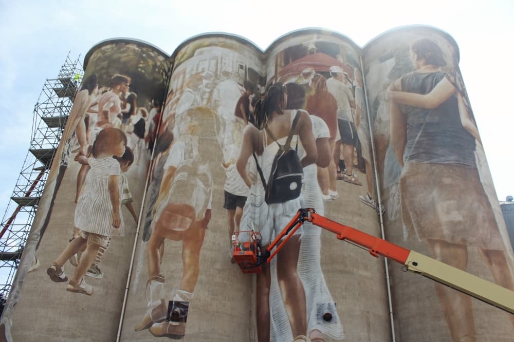 Guido van Helten paints a mural while on a mechanical lift. 