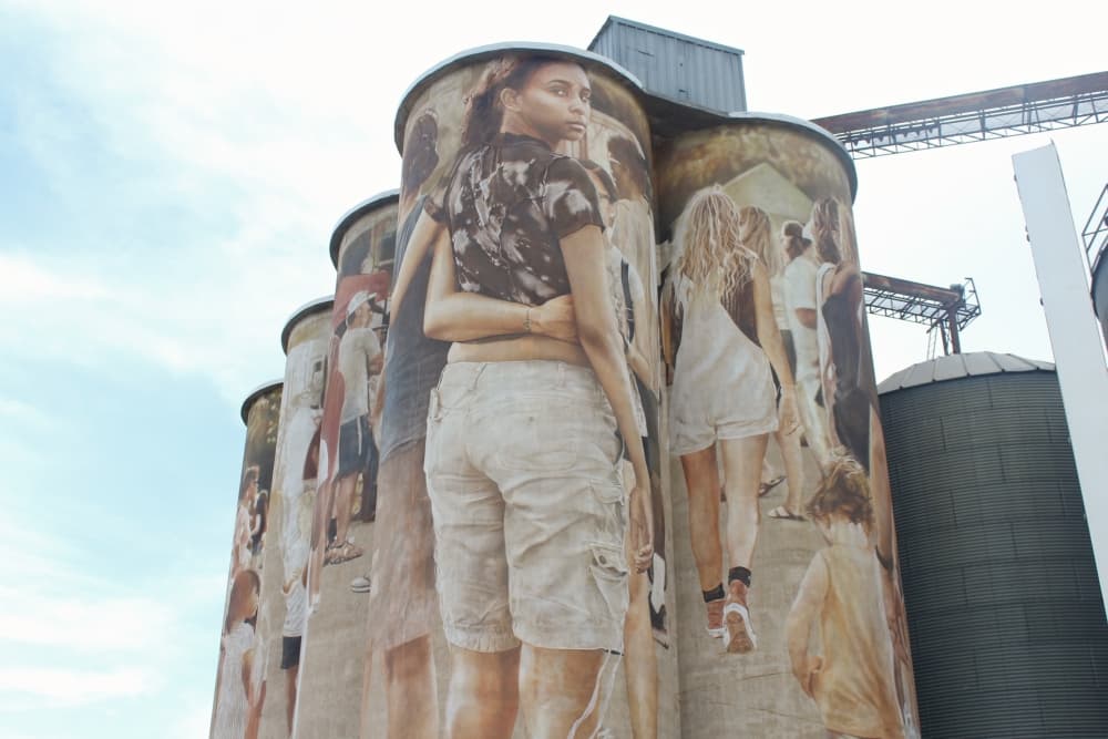 The short end of the silo mural depicting a girl in a crowd looking back and showing her face.
