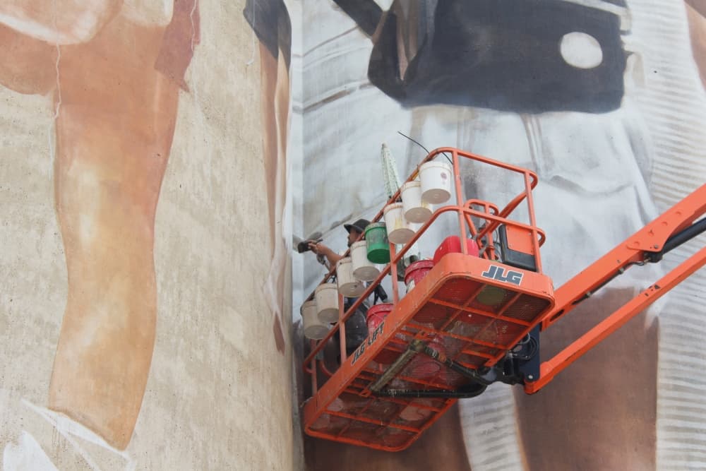 Guido van Helten paints a mural while on a mechanical lift. 