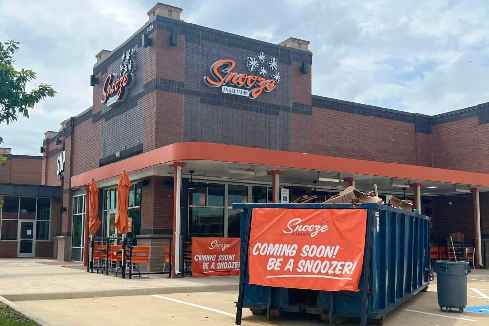 Building front of Snooze Eatery in Frisco with dumpster and a sign that says "Coming soon, be a snoozer"