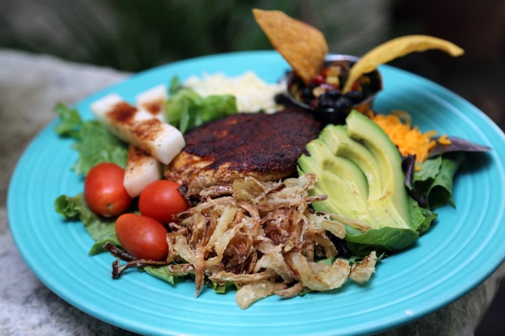 The Southwest Blackened Chicken Salad ($12) is served with fried onion chips, tomato, sliced avocado, crunchy lime jicama sticks and black bean salsa. (Courtesy Huisache Grill)