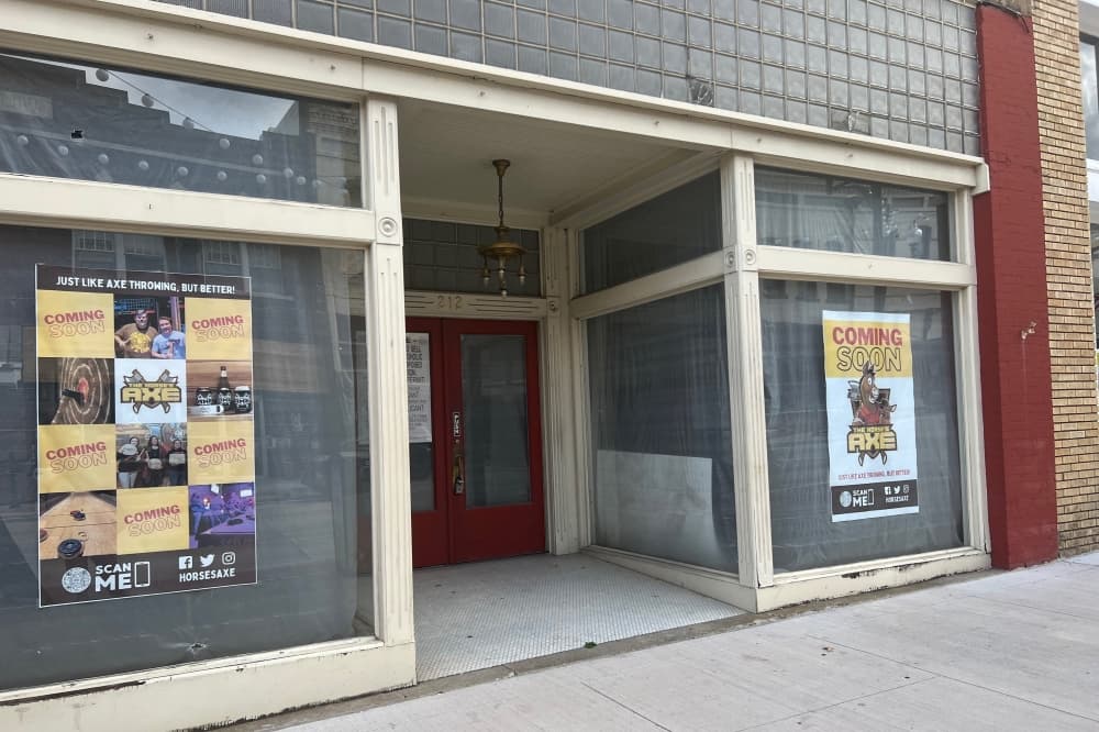 Storefront with covered windows and two "The Horse's Axe" coming soon posters.