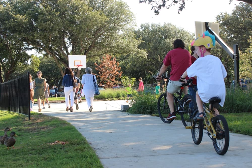Children ride their bikes past some ducks at the ribbon cutting ceremony at the newly renovated Rheudasil Park. (Samantha Douty/ Community Impact Newspaper)