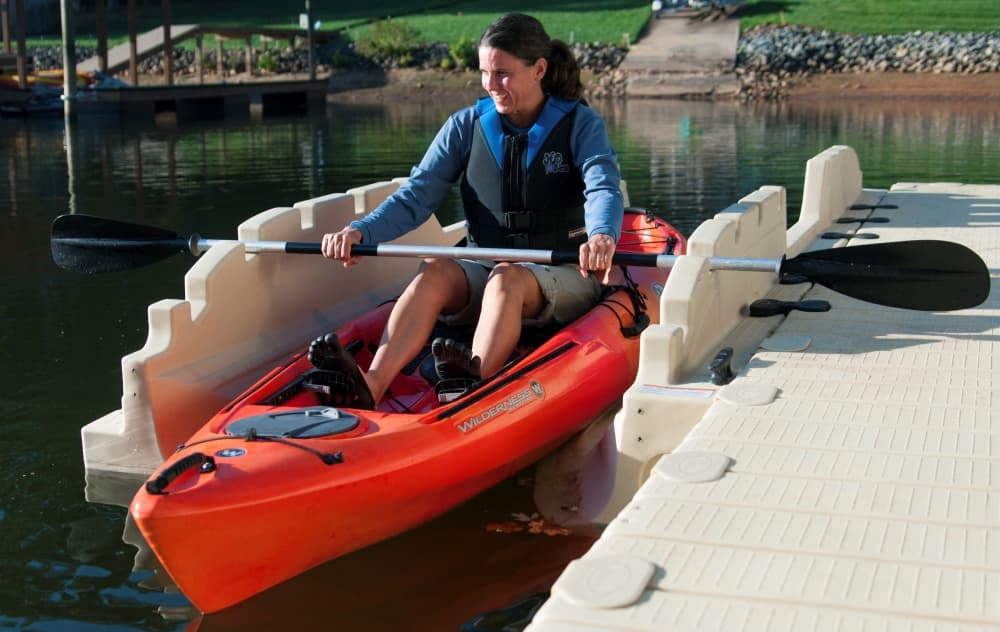 A woman in a kayak utilizing a kayak launch on the edge of a floating dock.