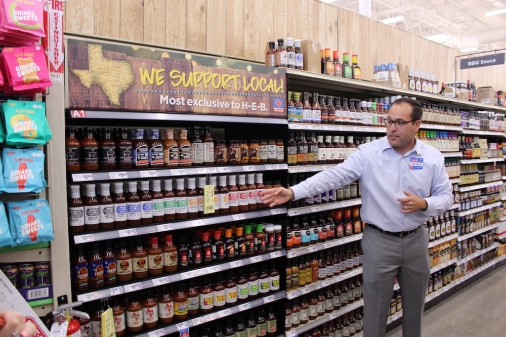 H-E-B Executive Vice President Juan-Carlos Ruck showcases the section of local barbecue sauces offered at the H-E-B store in Frisco. (Colby Farr/Community Impact Newspaper)