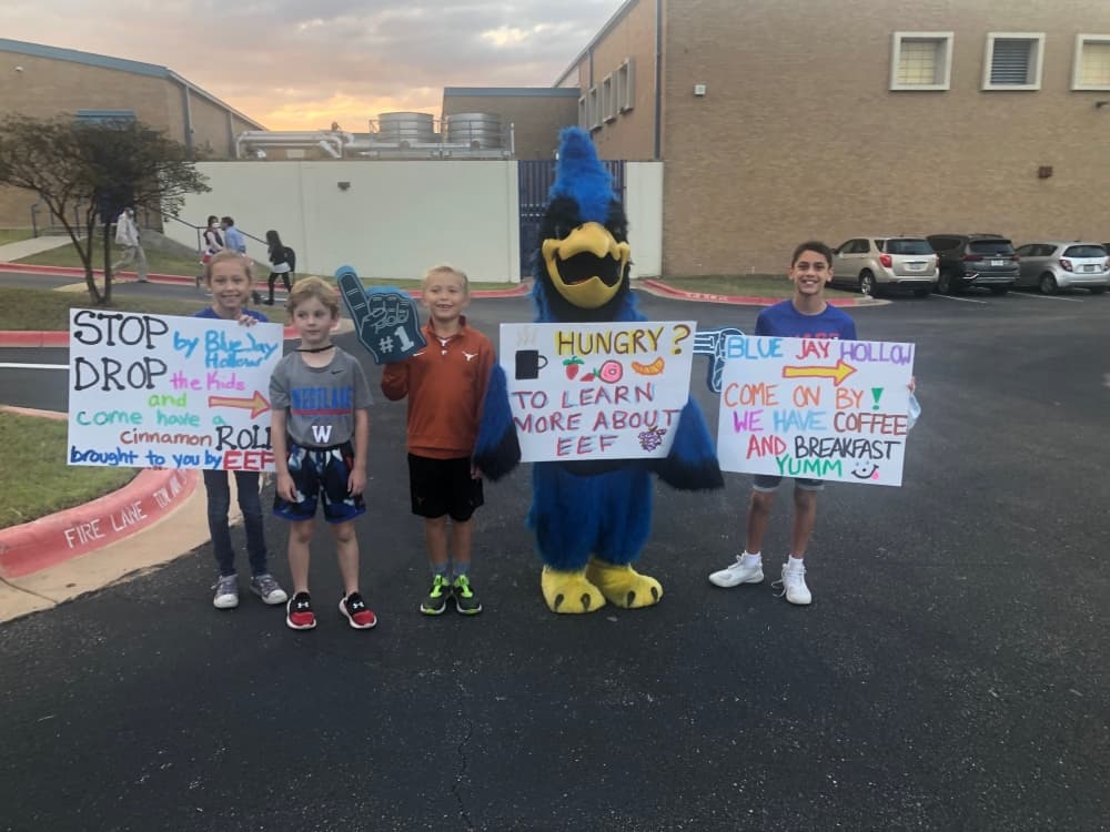 three kids with signs standing with blue bird mascot 