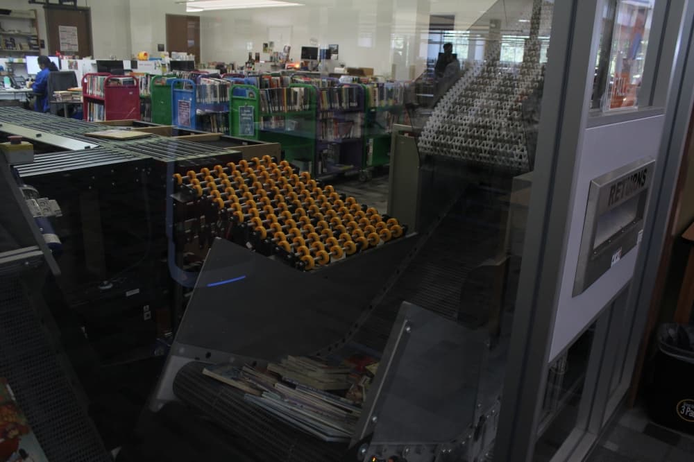 A stack of books being transported on the conveyor belt of the automated materials handler.