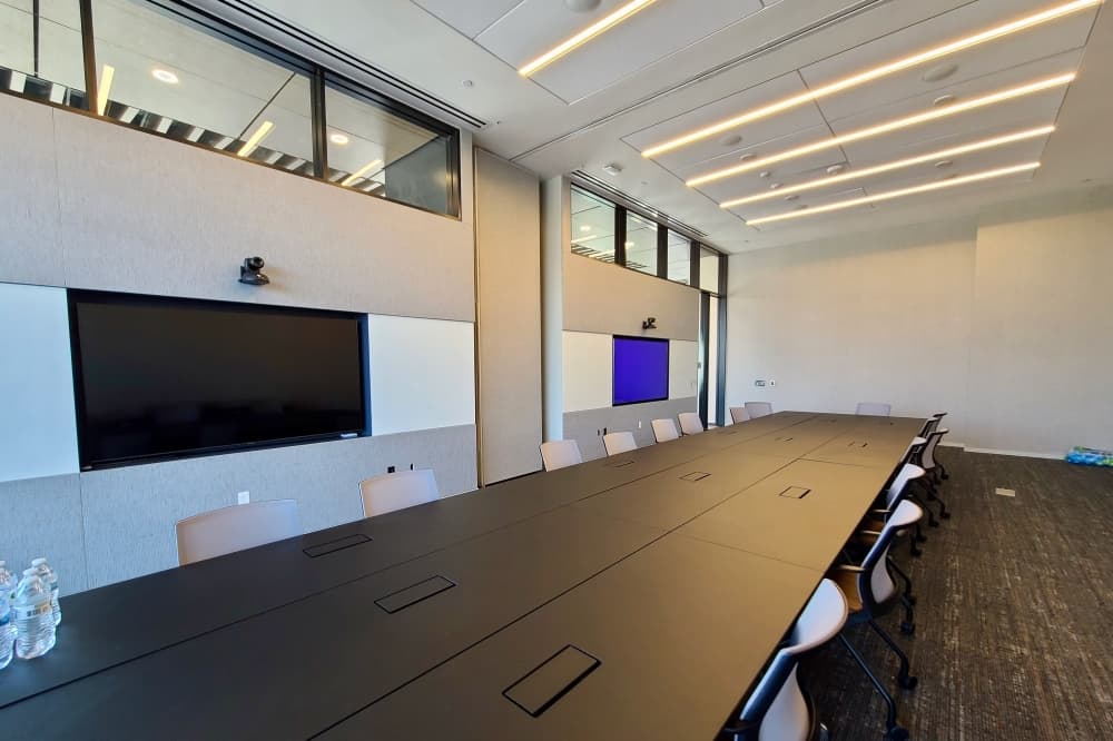 Meeting room with long table and chairs, and screens on the wall.