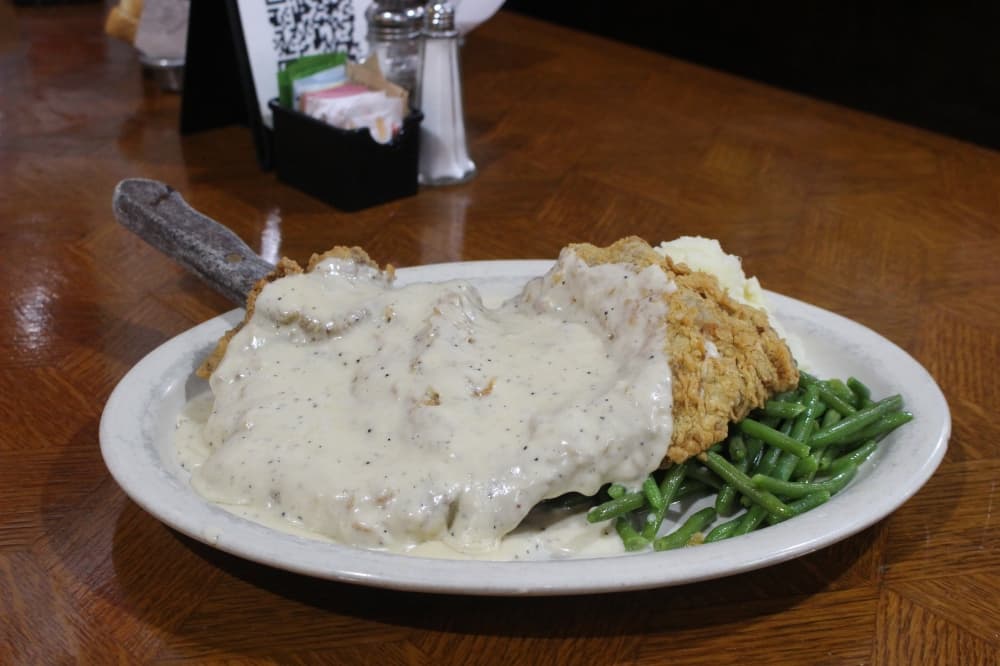 The chicken-fried steak ($17.99/$23.99) is served with roasted garlic mashed potatoes, French green beans and a homemade pepper cream gravy. (Kylee Haueter/Community Impact)