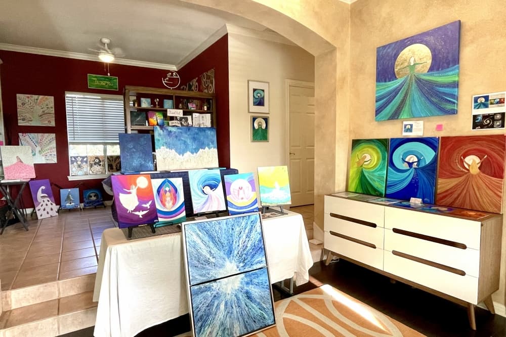 Numerous paintings displayed on tables and walls.