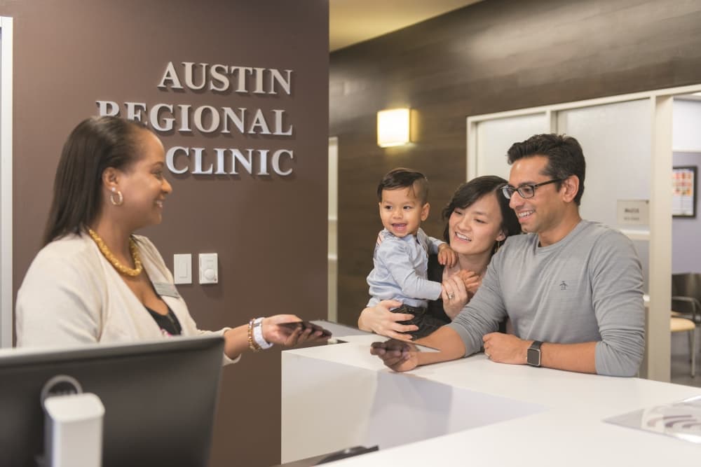 A woman behind a counter talking to a man, woman and baby in their arms