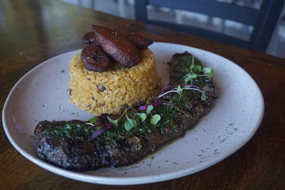 Churrasco grilled skirt steak is served with two sides. Arroz con Gandules and Maduros are pictured. (Mikah Boyd/Community Impact)