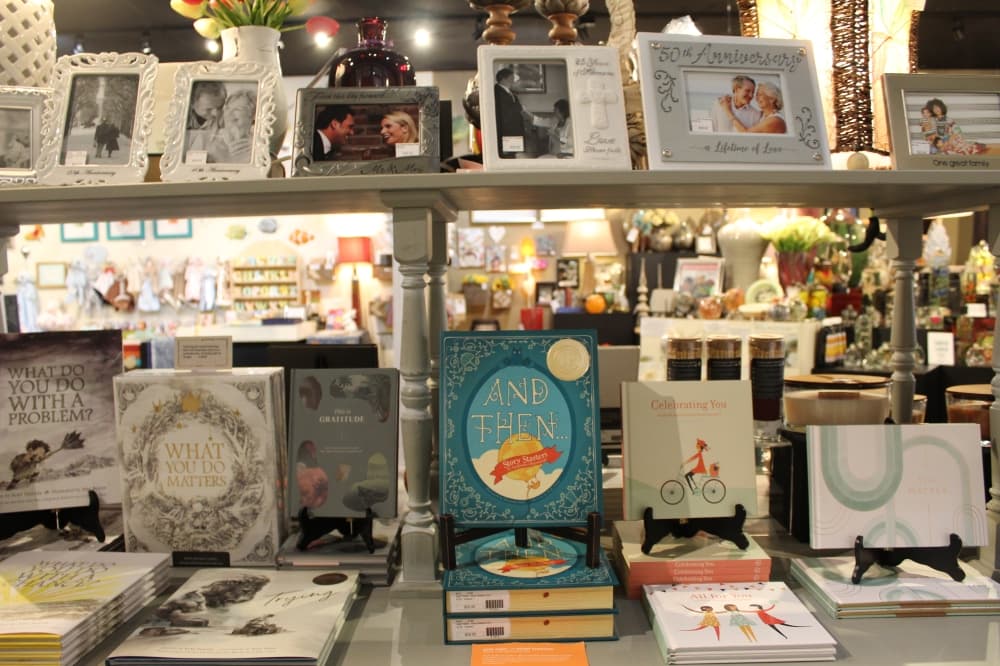 A corridor toward the back of the shop features a wall of gifts cards on one side and a table of books on the other. 