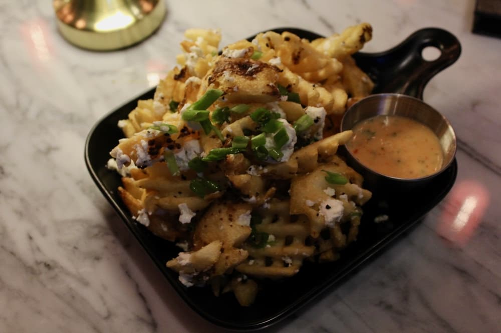 The truffle waffle fries ($10) are topped with goat cheese, black truffle oil, scallions and herbs, and are served with Thai chili aioli. (Shelbie Hamilton/Community Impact)
