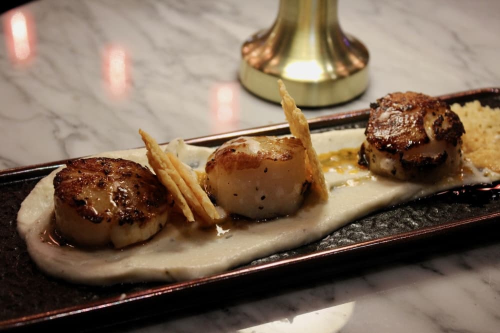 The seared scallops ($30) are served with a cauliflower puree, crispy sun chokes and chili oil. (Shelbie Hamilton/Community Impact)
