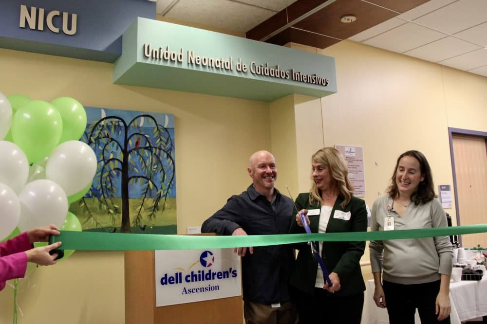 Two women and one man cutting a ribbon with balloons on the side
