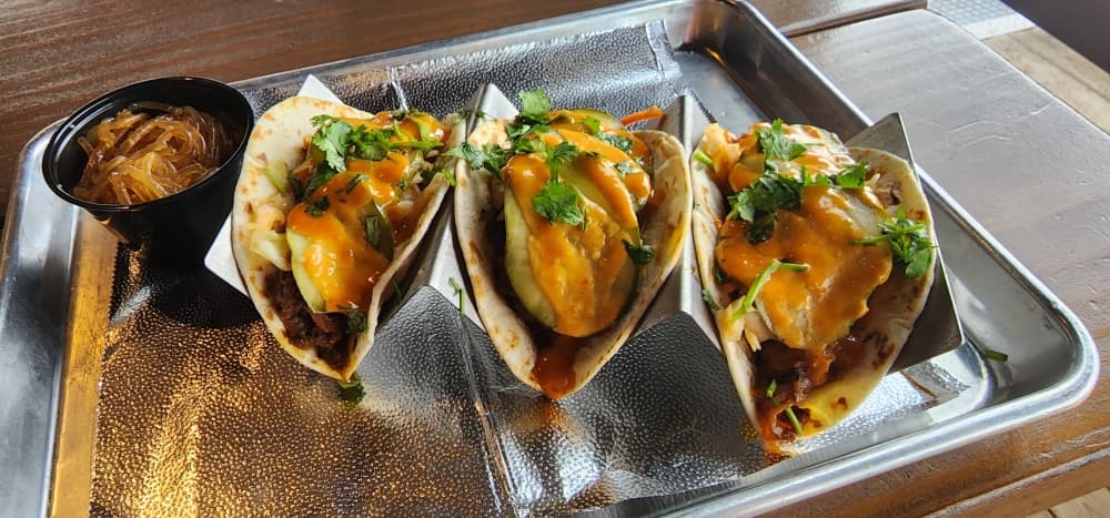 The Korean Brisket Tacos (3) are three flour tortillas filled with slow-cooked braised Korean brisket, kimchi slaw, sunomono pickled cucumbers, fresh cilantro, and gochujang mayo served with a side of Korean sweet potato noodles. (Jarrett Whitener/Community Impact)