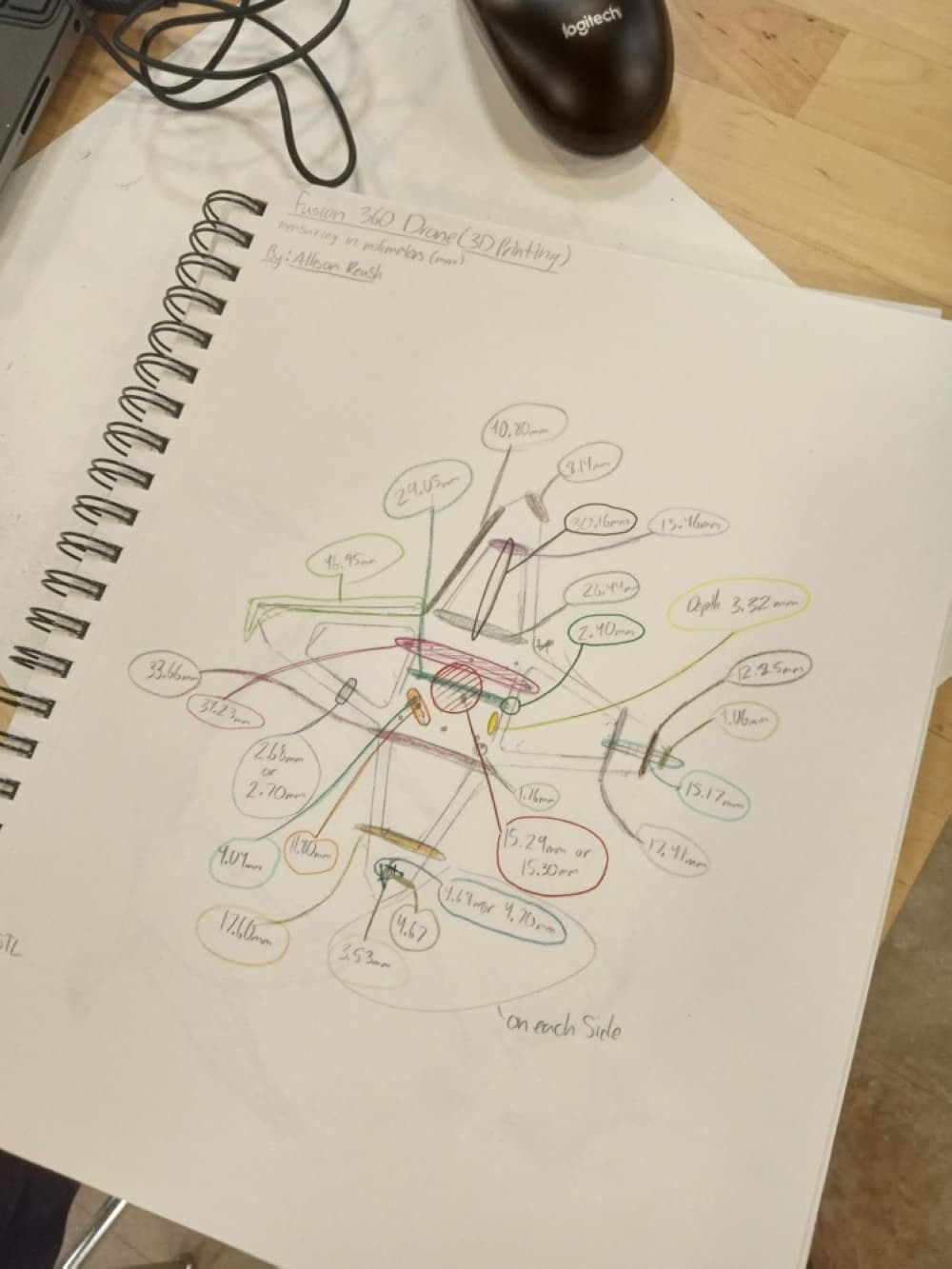 a sketchbook on a table opened up to a page of a drawing of a drone with its parts labeled 