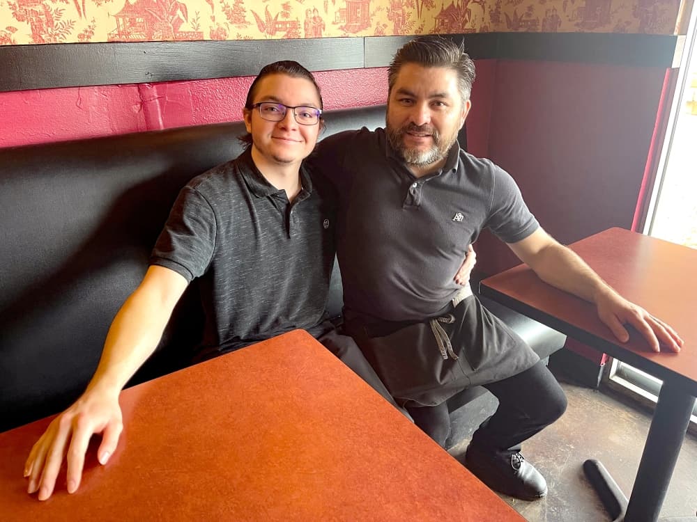 server son devon and owner leo ponce sit at booth in shaghai express restaurant smiling for photo