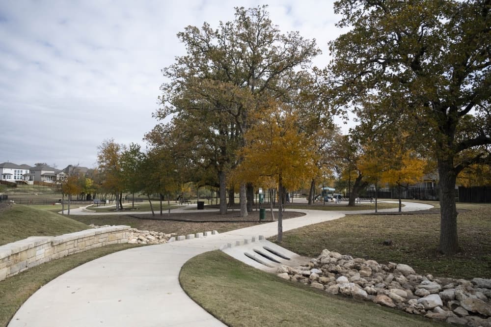 sidewalk winding through green space with trees that have autumn colored leaves