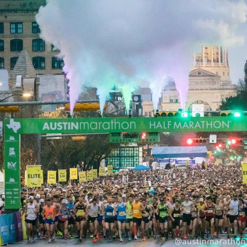 hundreds of marathon runners stand at the starting line on congress avenue in front of the texas state capitol building