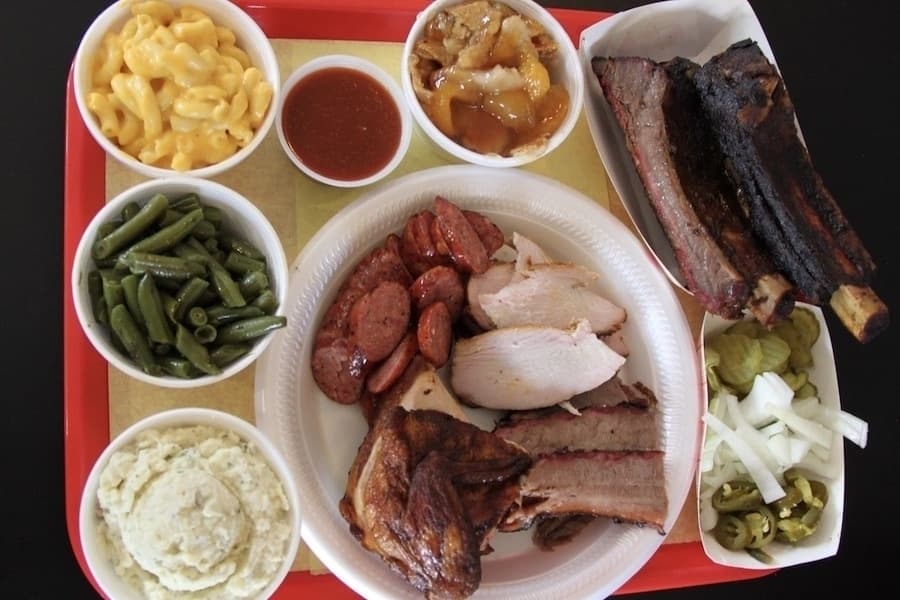 tray of food with beef ribs, turkey, barbecue chicken, brisket, mac and cheese, potato salad, green beans, dessert, barbecue sauce
