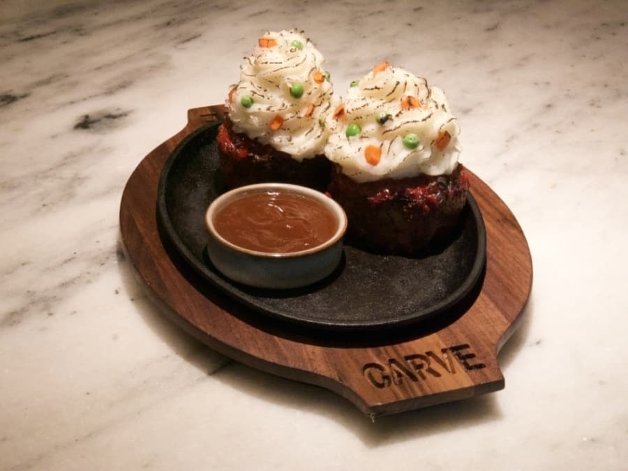 two wagyu meatloaf pieces with mashed potatoes on top to resemble cupcakes and peas and carrots to resemble sprinkles