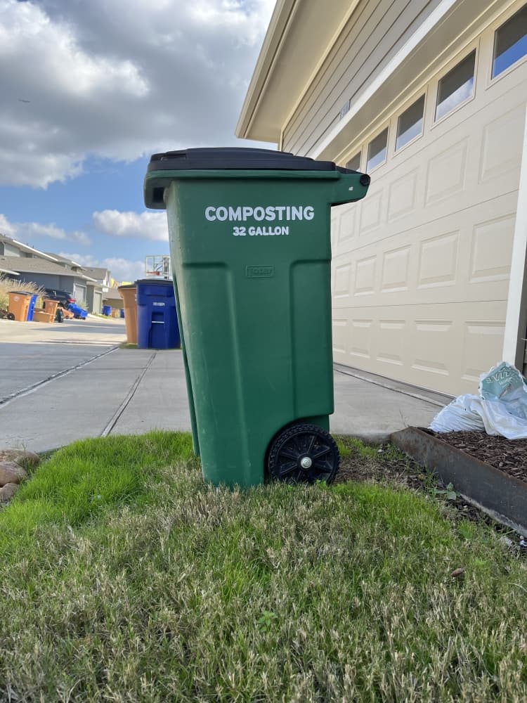 green composting bin sits outside garage on patch of grass