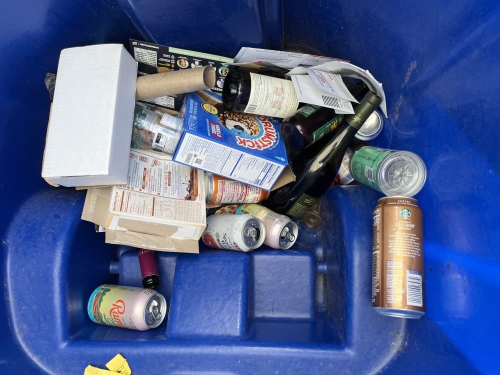 inside of a recycling bin with soda cans, boxes, wine bottle and other recycling products