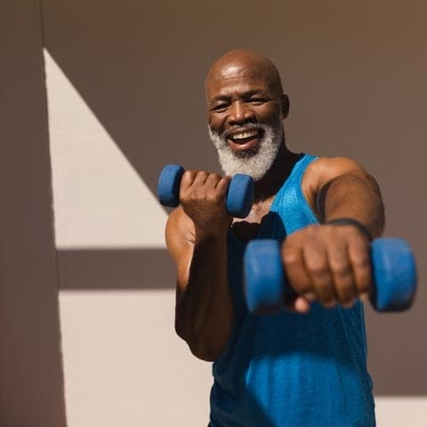 Front view of active senior African American man training arms with dumbbells in the backyard of home
