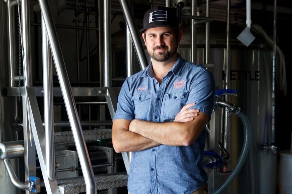 Owner Bryan Winslow stands with his arms crossed next to the distillery for a photo