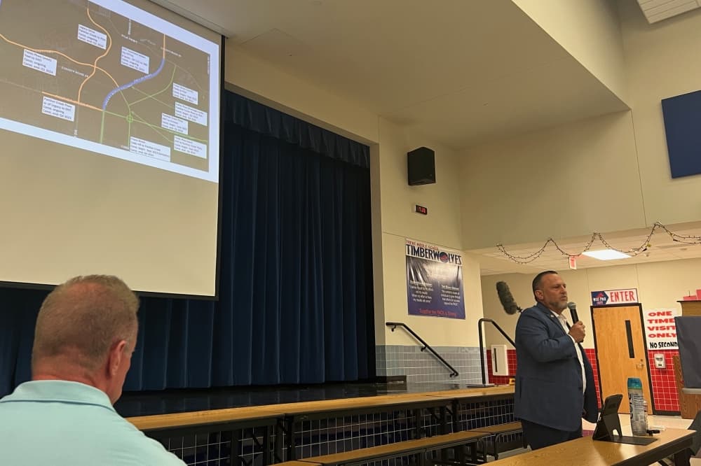 John McReynolds holding a microphone in front of a projected screen with a map.