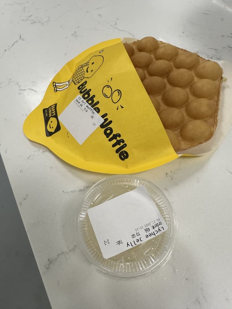 A waffle in a paper jacket and a cup with topping.