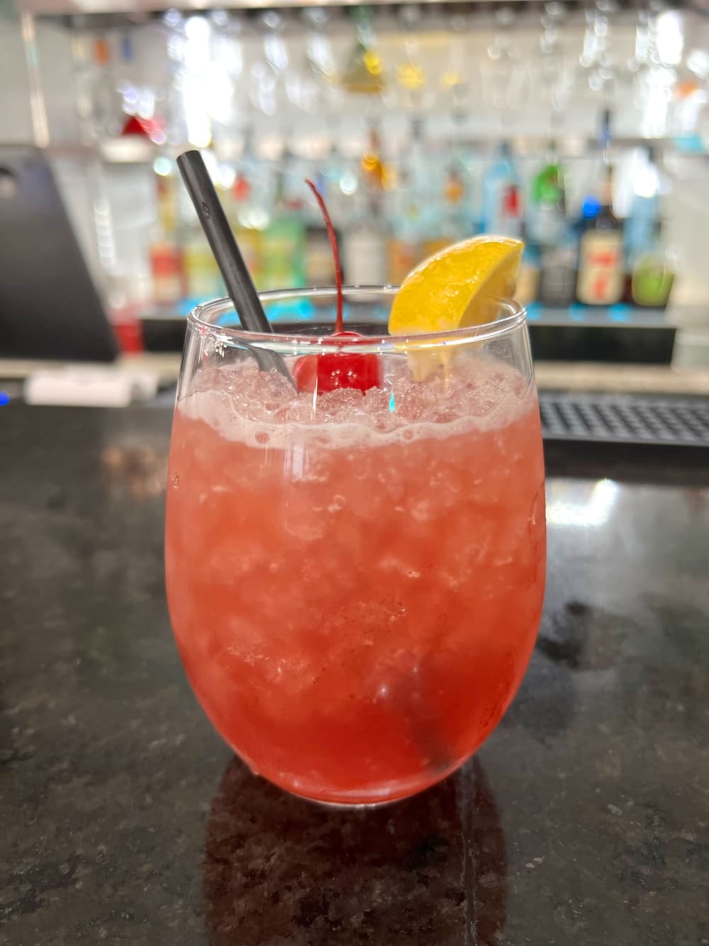 pink drink in wine glass with straw and cherry and lemon