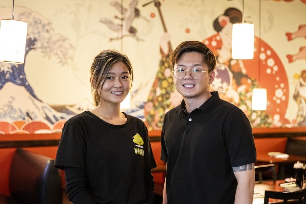 owners smile for photo in restaurant in front of mural