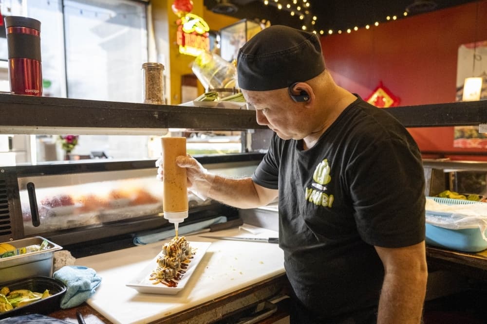 chef drizzles sauce over sushi roll in restaurant 