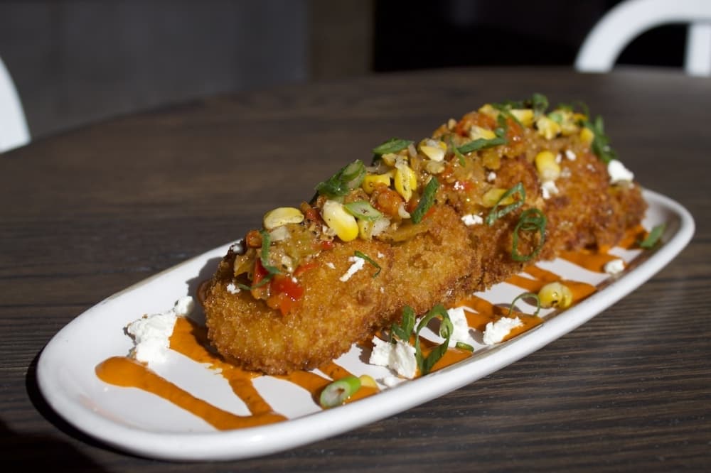 Fried green tomatoes are panko breaded with a red pepper tahini sauce, roasted corn sofrito, goat cheese and green onion. 