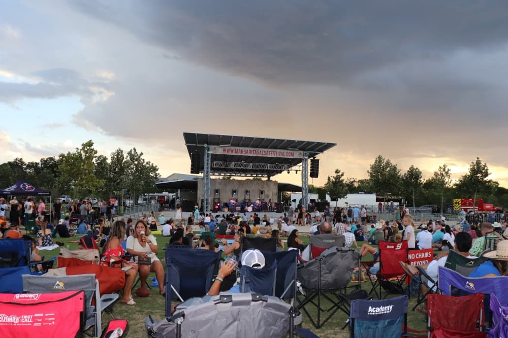 large crowd sits in fold-up chairs listening to performers on a stage