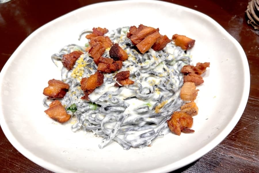 The squid ink carbonara comes with English peas, asiago cream and cured egg yolk topped with pork belly ($17). (Zara Flores/Community Impact)