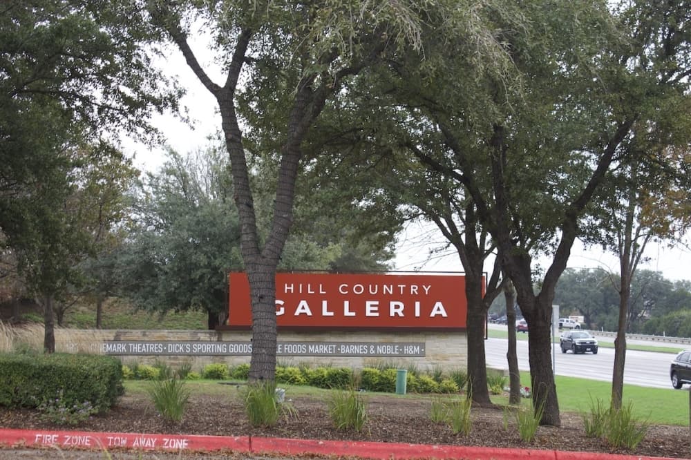 hill country galleria welcome sign covered with trees